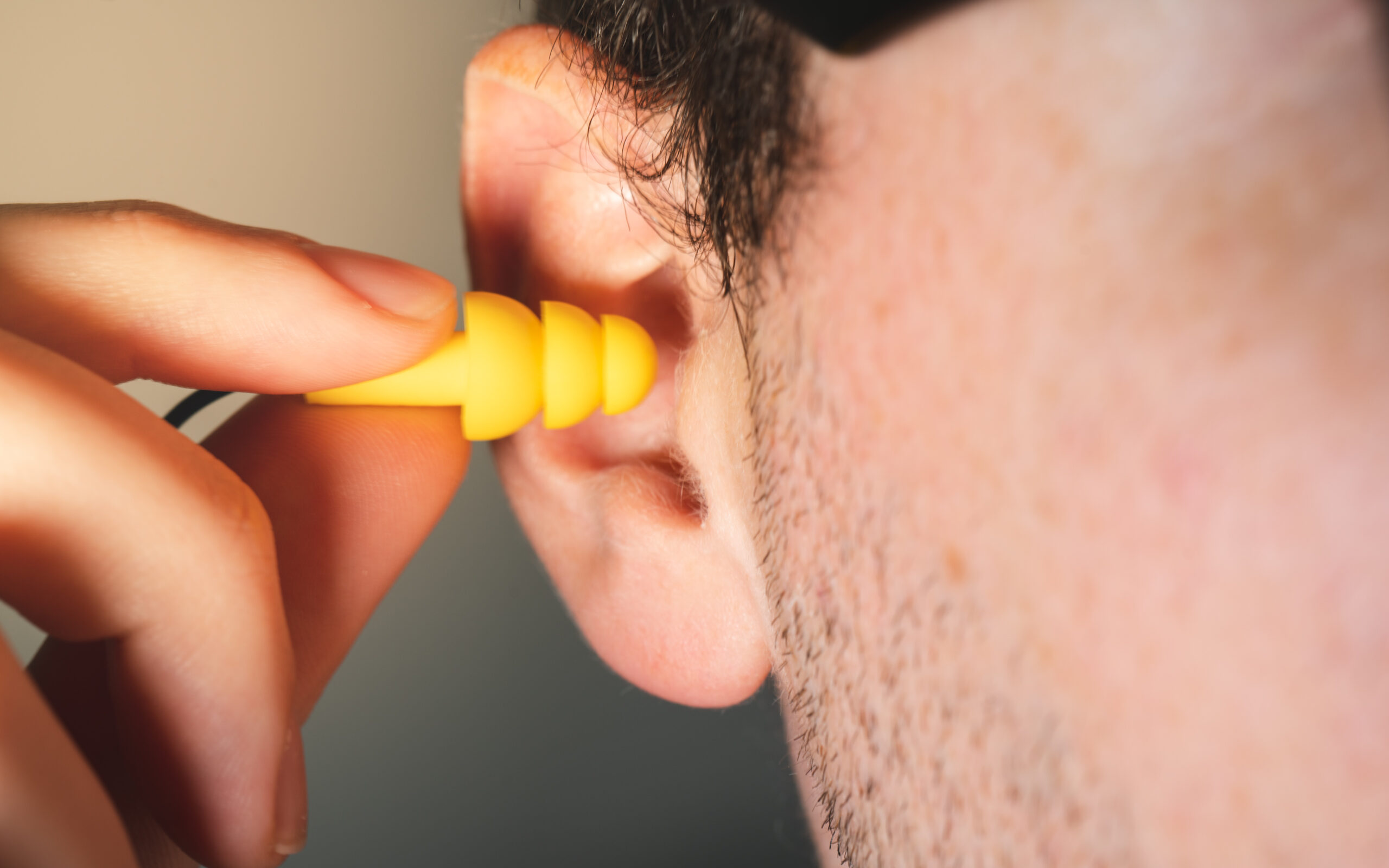 Man worker inserting yellow hearing safety protection earplug in his ear close-up view