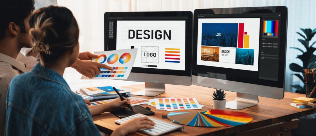 Two designers reviewing color palettes and logo layouts on dual monitors